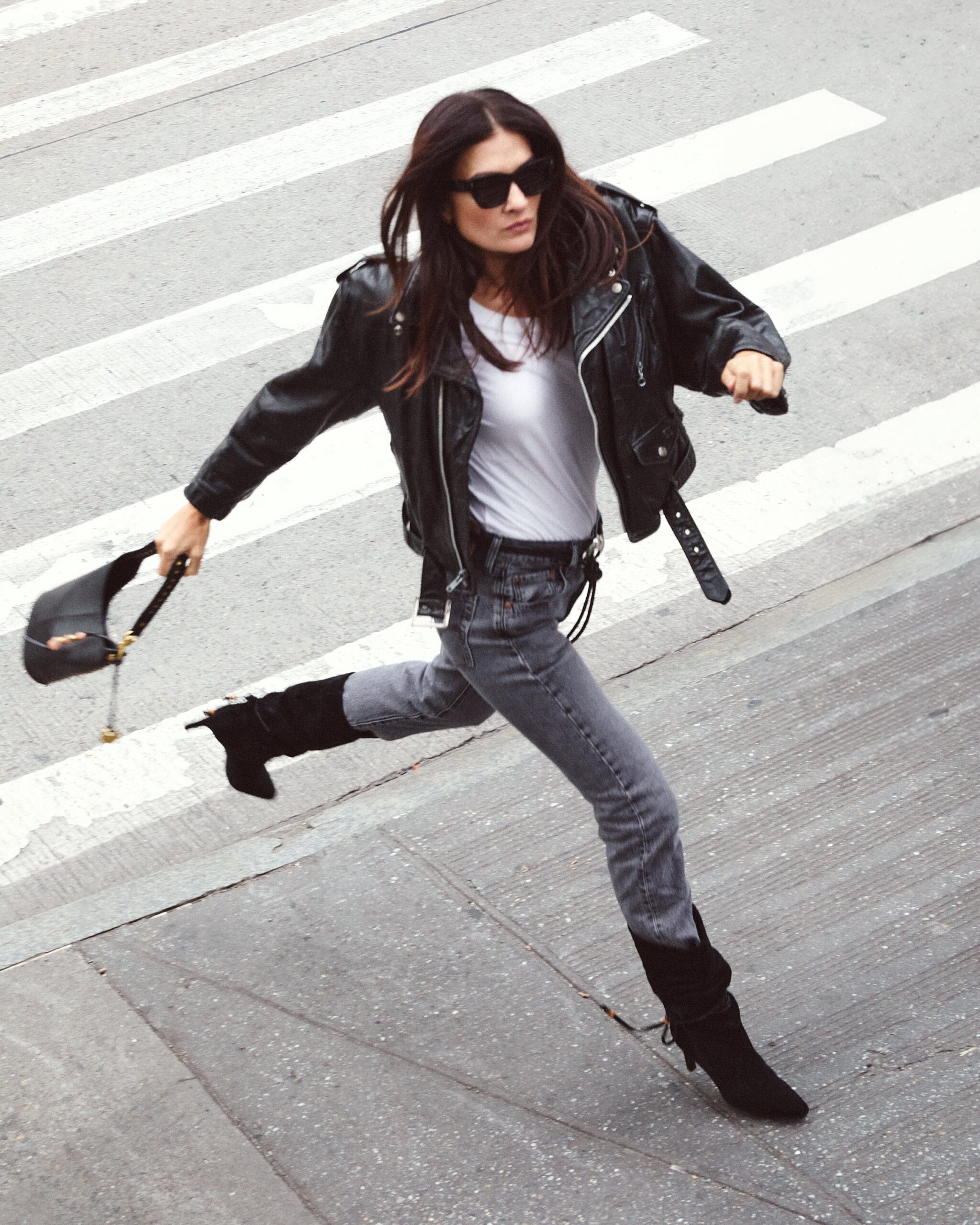 Woman in black leather jacket and ripped jeans running across crosswalk