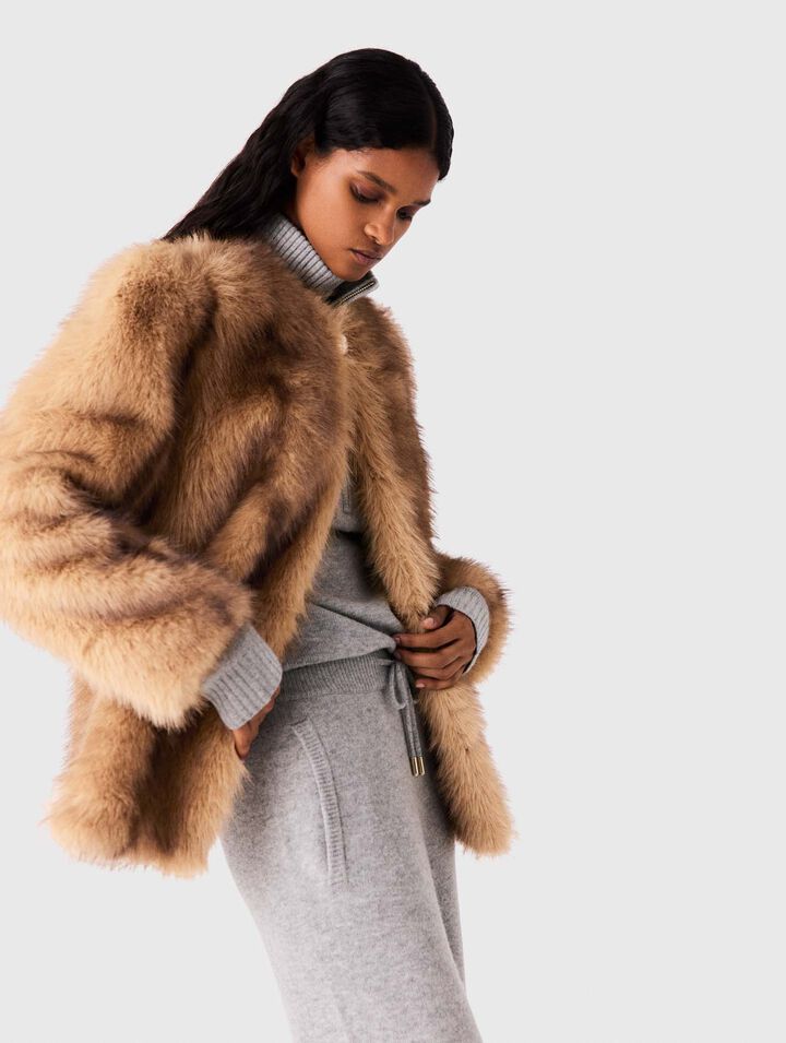 Woman adjusting camel fur stole over gray knit sweater and joggers