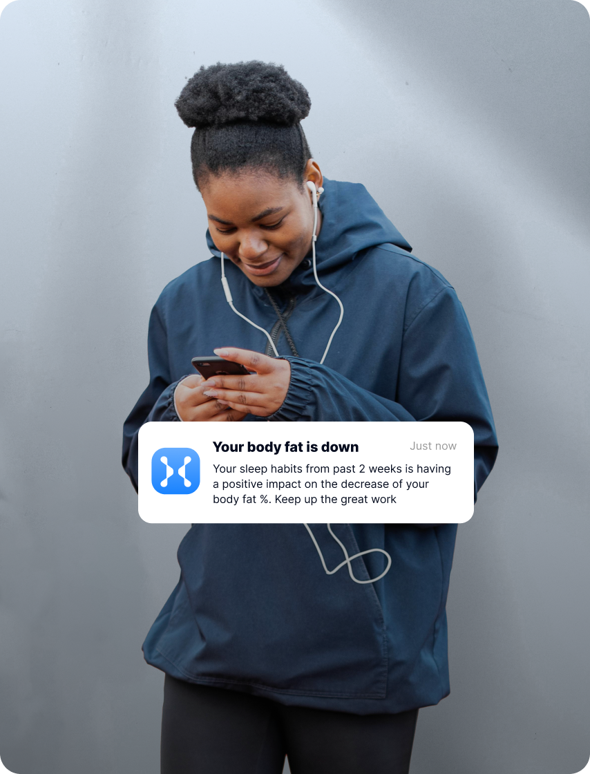 Woman in dark blue jacket holding smartphone with health app notification about body fat decrease