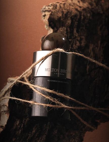 Dark fragrance bottle wrapped with twine against a textured brown and rust-colored artistic background