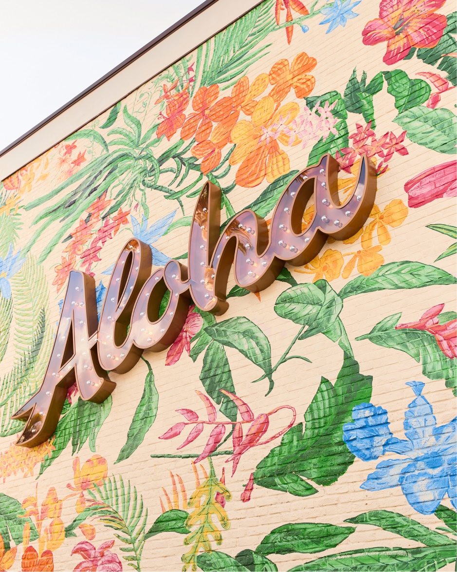 Storefront sign reading "Tommy Bahama" with colorful hand-painted tropical flowers