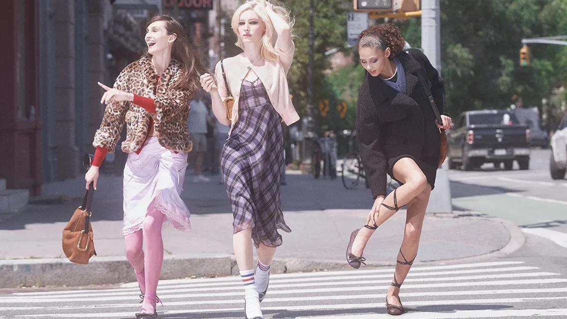 Three women crossing a city street wearing colorful vintage-inspired outfits with 1990s styling