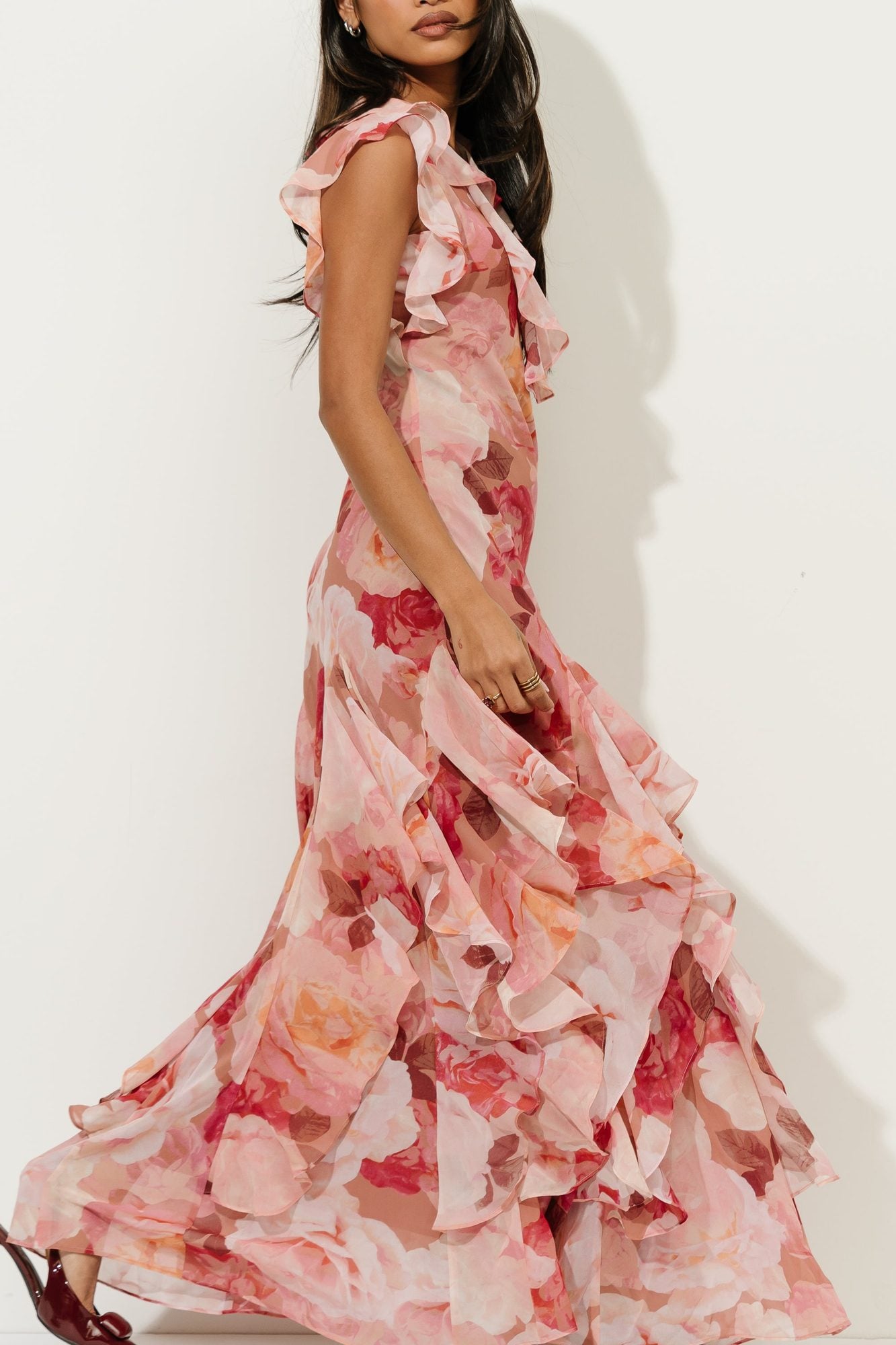 Woman in pink floral ruffle gown viewed from side, showing layered skirt detail