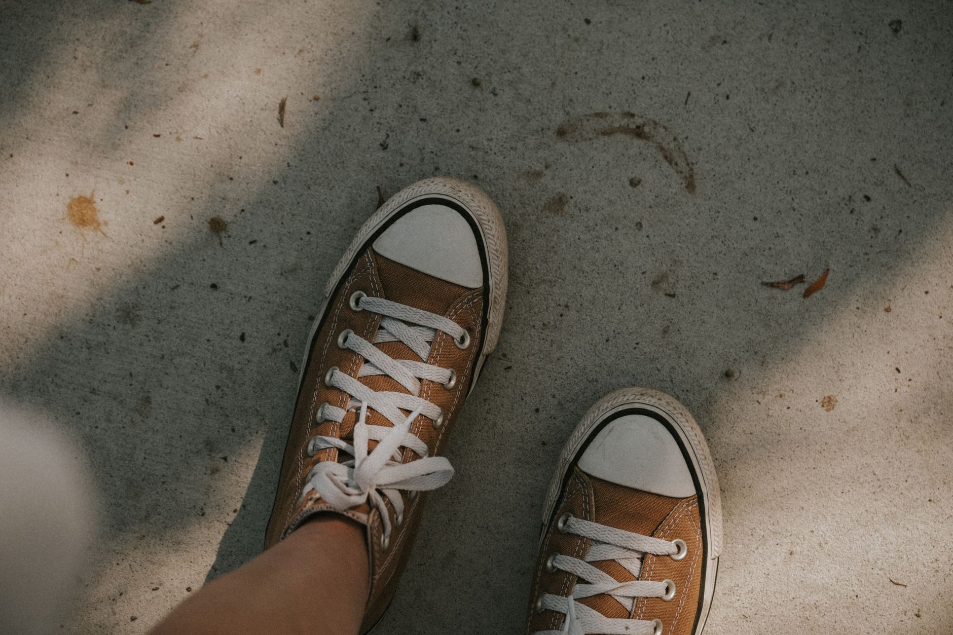 Overhead view of tan canvas high-top sneakers with white laces on concrete ground
