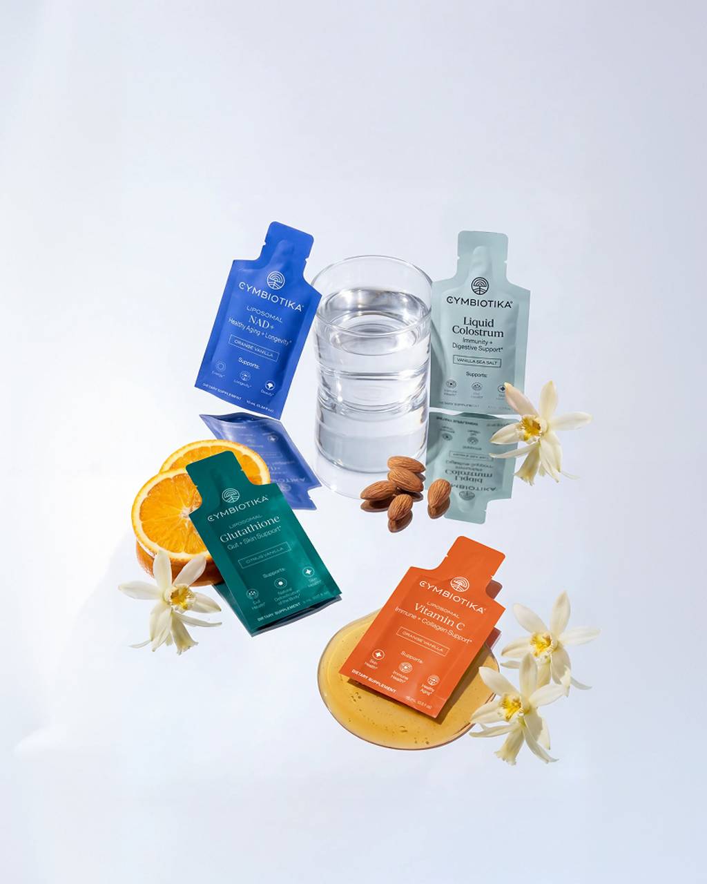 Assorted supplement packets and pouches arranged with water glass, almonds, and white flowers