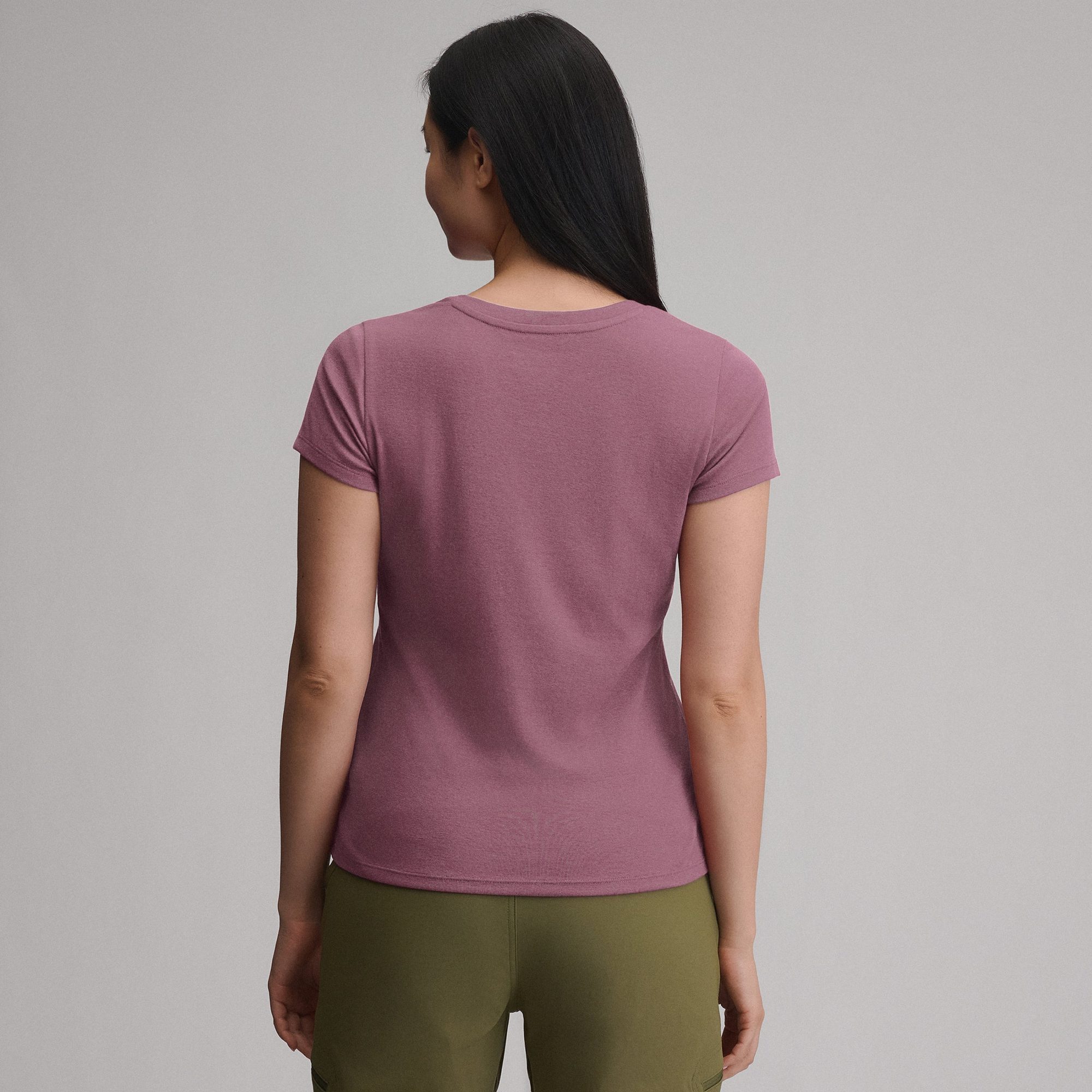 Woman wearing mauve v-neck t-shirt with olive green pants, back view against gray background
