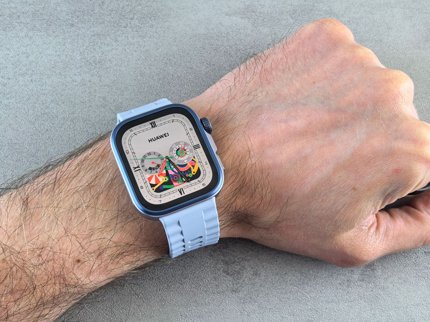 Light blue square smartwatch with colorful dial worn on person's wrist