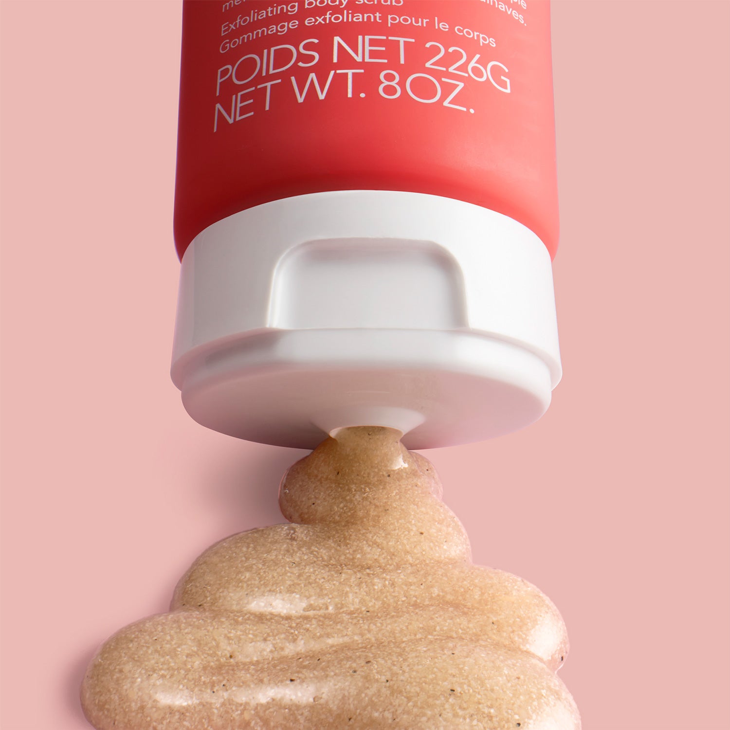 White tube cap with beige scrub texture squeezed out underneath on pink background