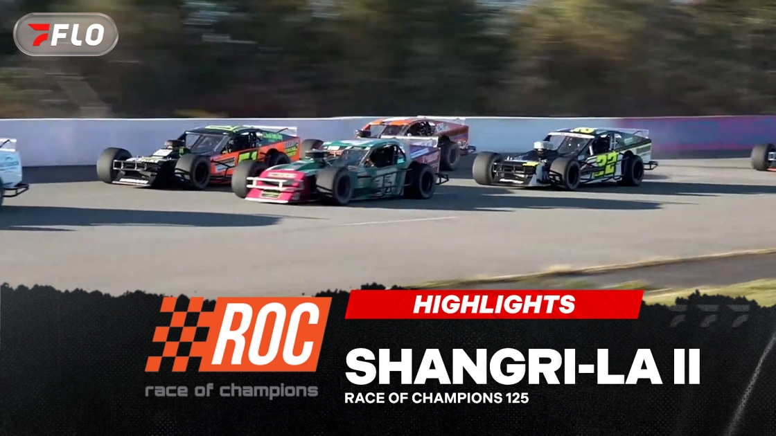 Multiple colorful race cars competing on paved oval track during daytime race
