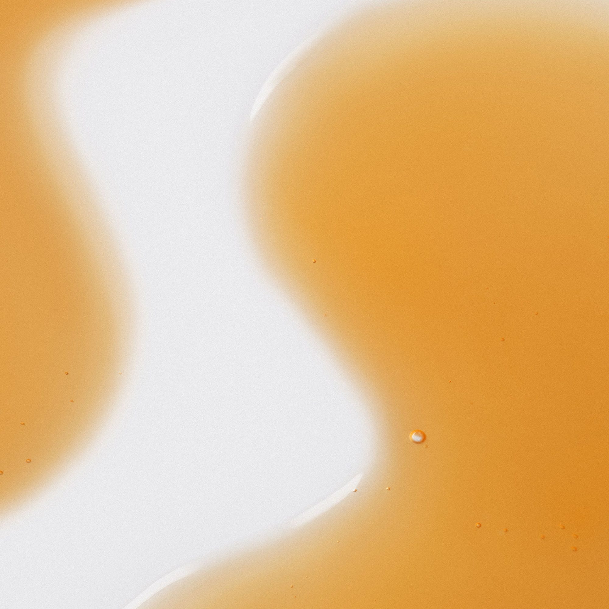 Golden liquid serum with a single droplet on peachy-toned background