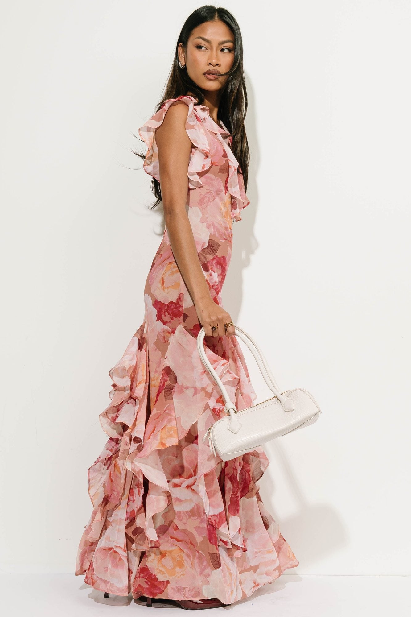 Woman in pink floral ruffle dress holding white shoulder bag, side view