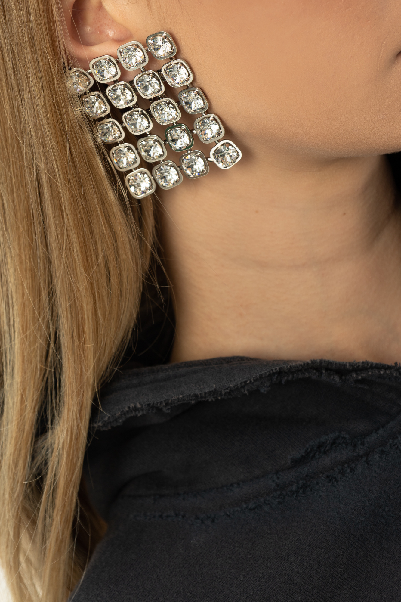 Woman wearing large rectangular crystal stud earrings against black clothing