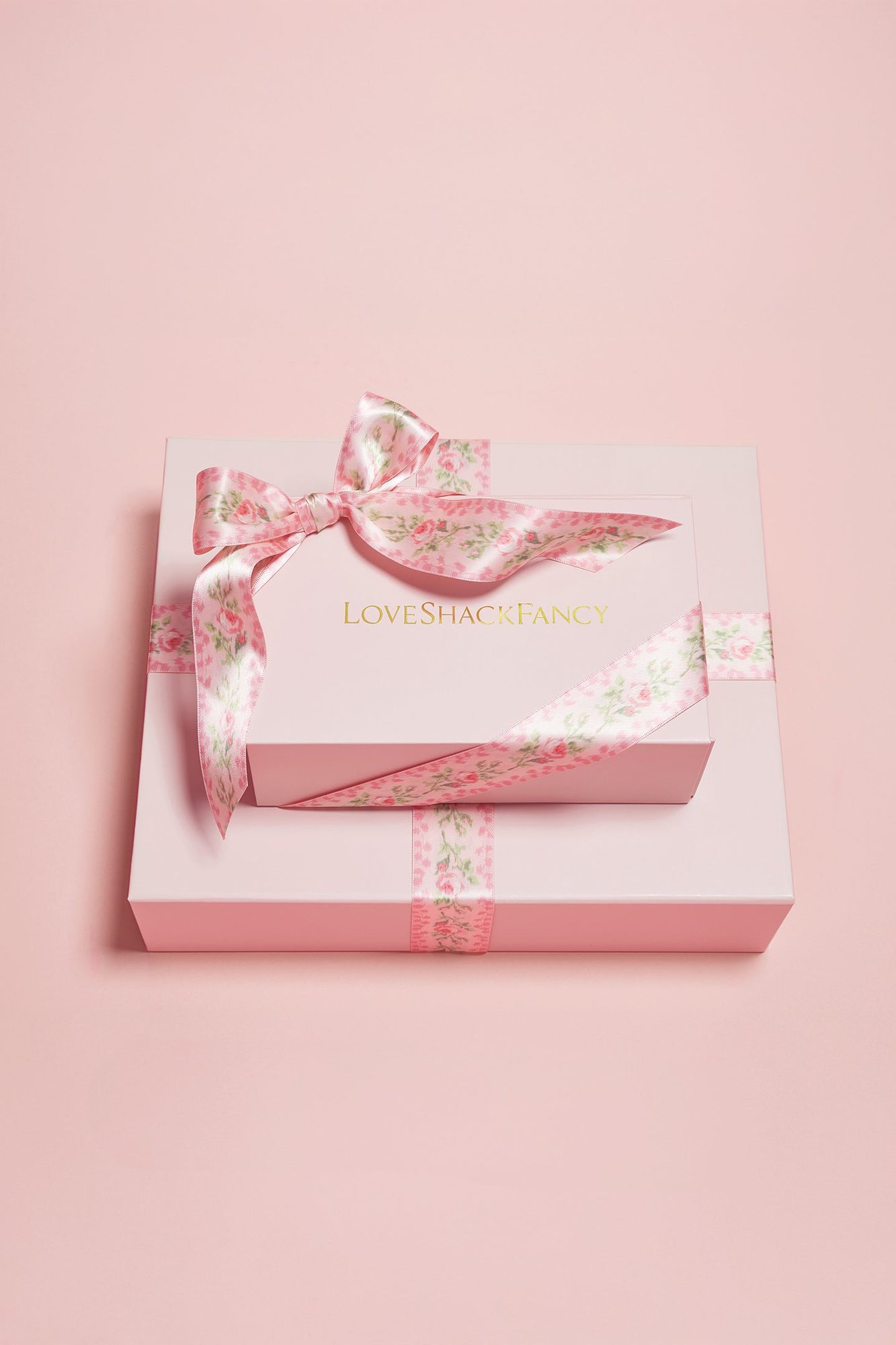 Pink and white gift box with floral ribbon bow and gold text on lid