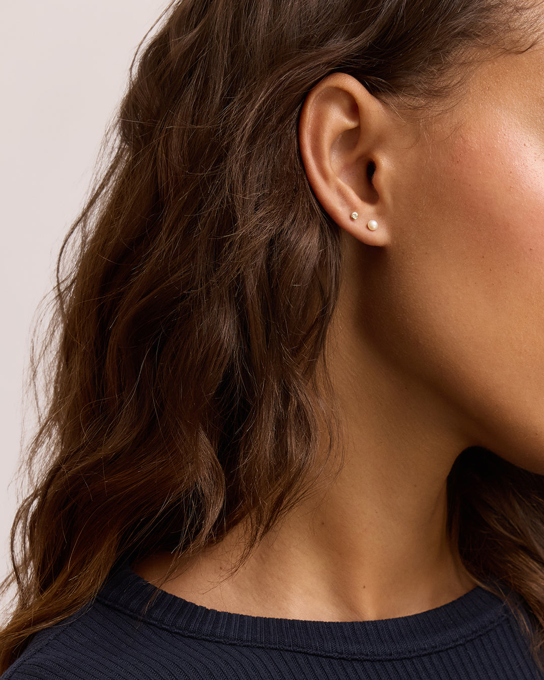 Side profile of woman's ear with two small pearl stud earrings