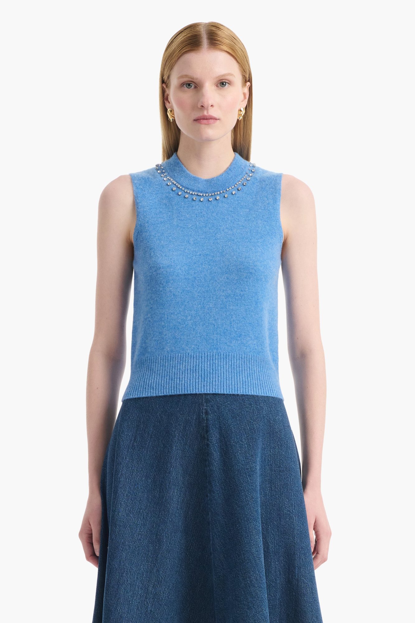 Woman in light blue sleeveless cashmere sweater with pearl beaded collar and dark denim skirt